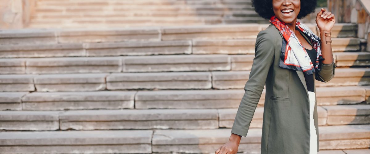 Fashionable girl in a summer city. Black lady in a green jacket. Woman in a red scarf. Famale with sunglasses